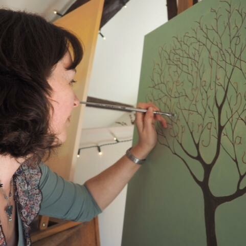 Charlotte Wakefield at her easel, painting letters into the branches of a tree on a green canvas